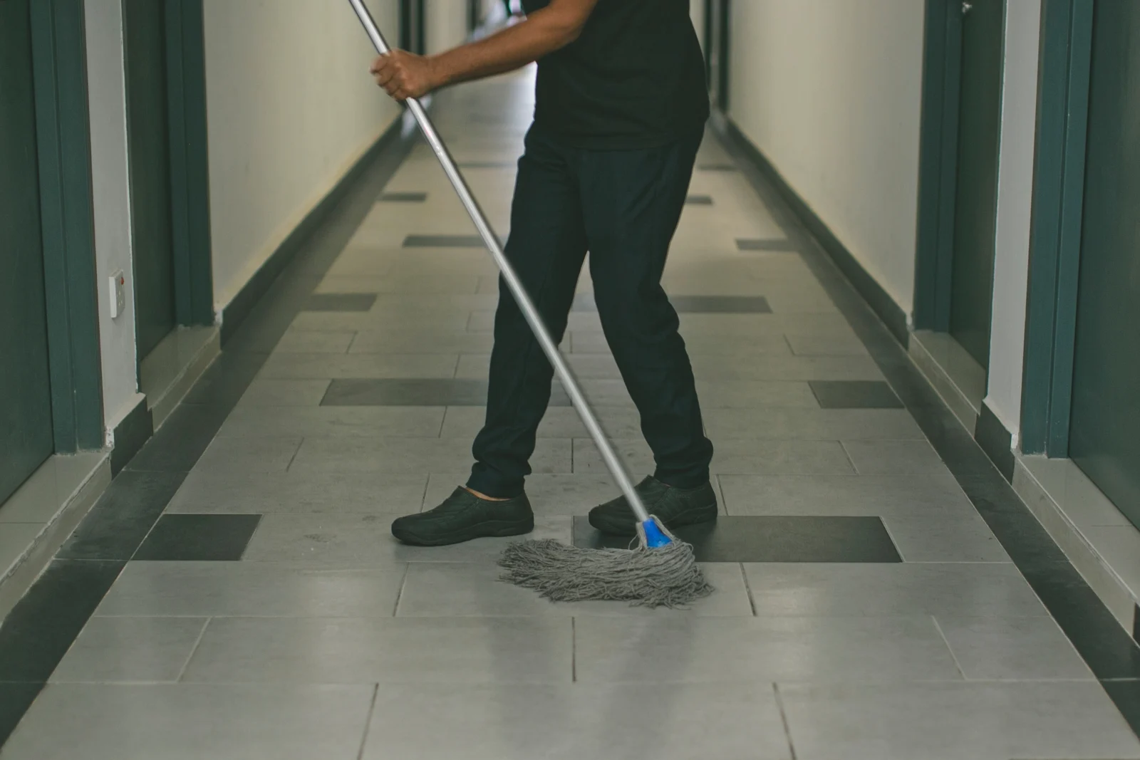 Profissional limpando o piso de um corredor com mop.